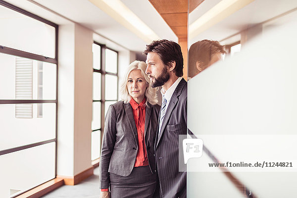Portrait of businesswoman and businessman looking out of office window