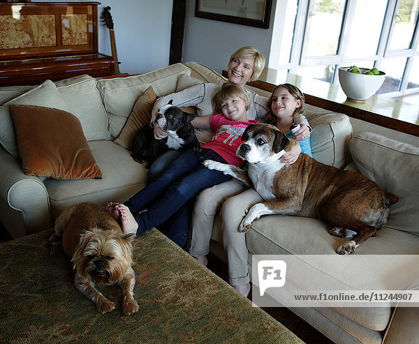 Mutter und Töchter sitzen mit ihren Hunden auf dem Sofa und sehen gemeinsam fern