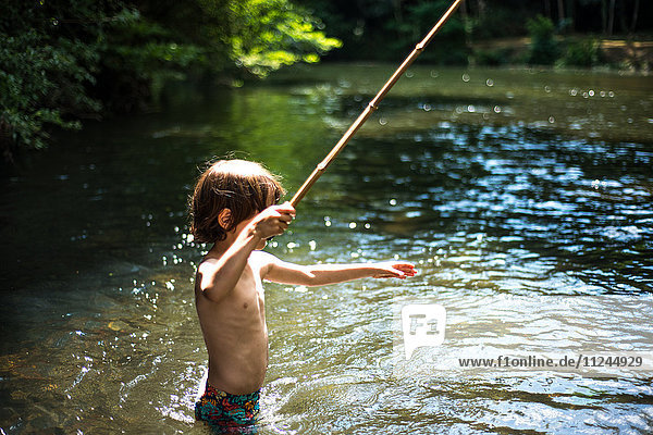 Junge mit tiefer Taille im Wasser hält Stock