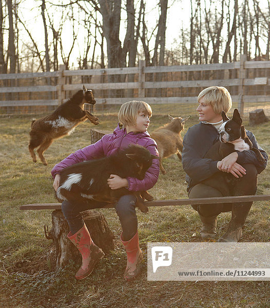 Mutter und Tochter im Freien  Ziegen und Haushund umarmend