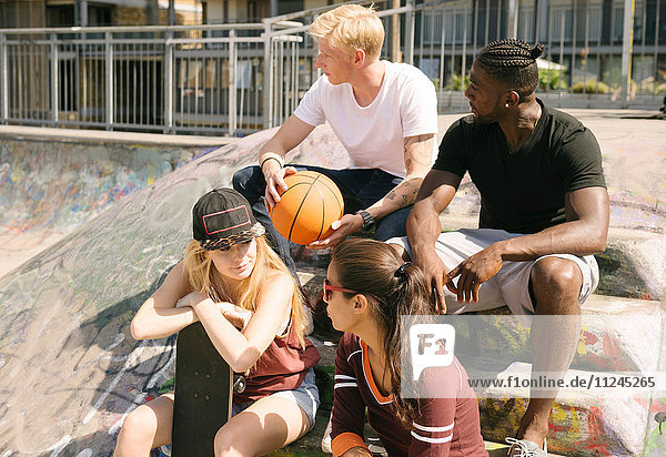 Männliche und weibliche Basketballfreunde unterhalten sich im städtischen Skatepark