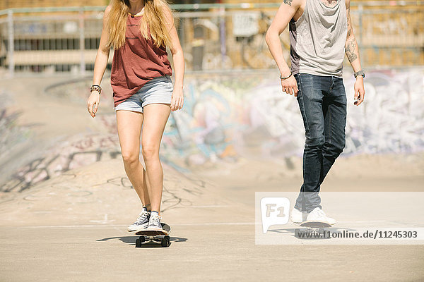 Neck down view of female and male skateboarders skateboarding in skatepark