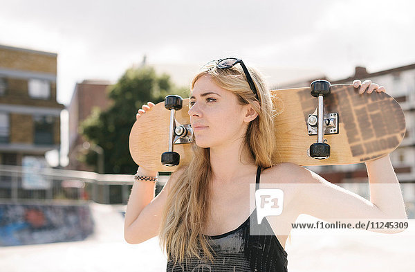 Junge Skateboardfahrerin trägt Skateboard auf den Schultern im Skatepark