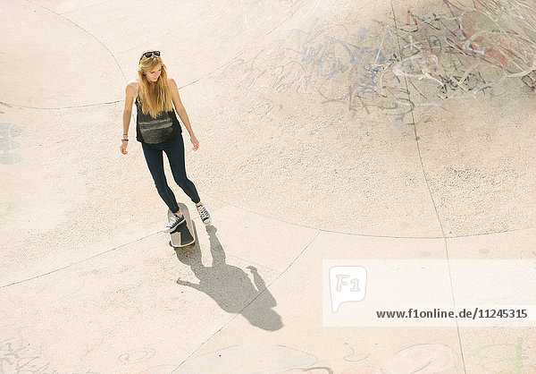 Hoher Winkel der jungen Skateboarderin beim Skateboarden im Skatepark