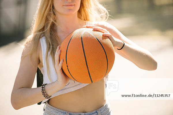 Mittlere Sektion einer jungen Frau beim Training auf dem Basketballplatz
