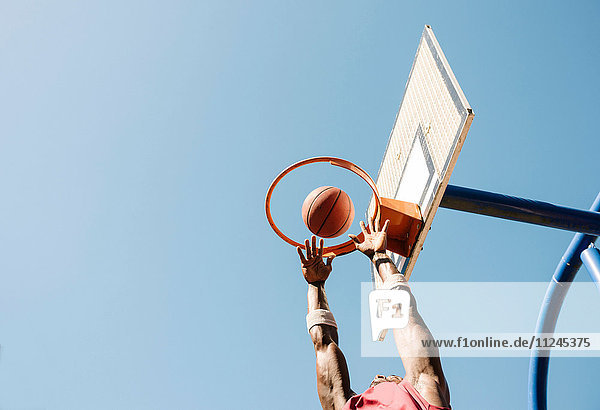 Junger männlicher Basketballspieler wirft Ball im Basketballkorb