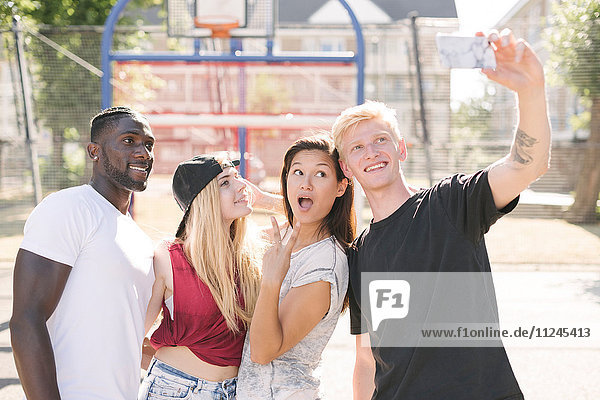 Vier erwachsene Freunde posieren für Smartphone-Selfie auf dem Basketballplatz