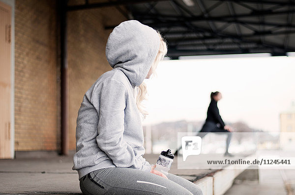 Female runner watching friend warming up outside warehouse