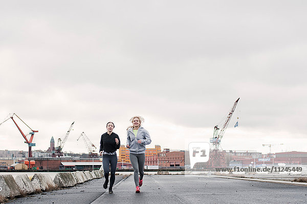 Two female running friends running along dockside