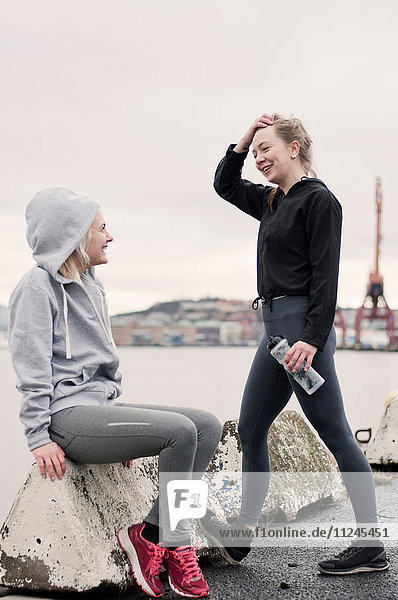 Two female running friends chatting on dockside