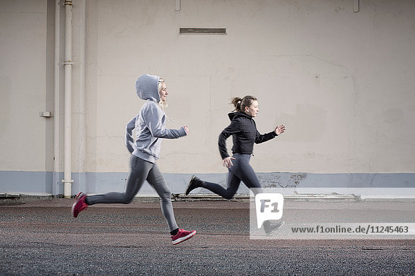 Two female runner friends running on urban road