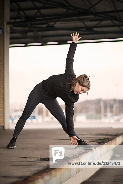 Female runner bending forward stretching on warehouse platform
