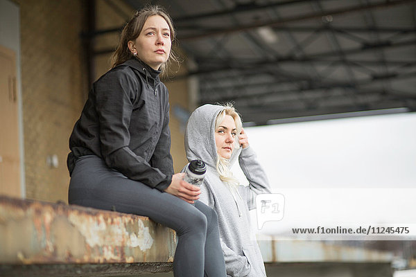 Two female runner friends looking out from warehouse platform