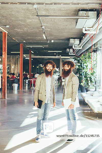 Porträt von männlichen erwachsenen Hipster-Zwillingen mit digitalem Tablett und Laptop im Büro