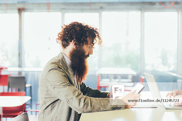 Junger männlicher Hipster mit lockigem Haar und Bart mit digitalem Tablett am Schreibtisch