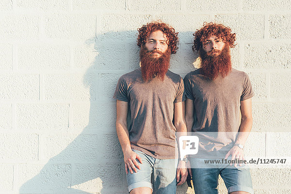 Portrait of identical adult male twins with red hair and beards against wall