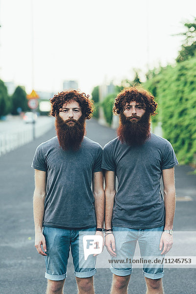 Porträt von eineiigen erwachsenen männlichen Zwillingen mit roten Haaren und Bärten auf dem Bürgersteig.