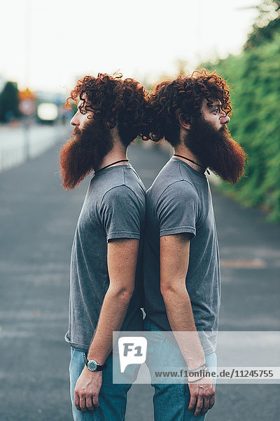 Porträt von eineiigen erwachsenen männlichen Zwillingen mit roten Haaren und Bärten Rücken an Rücken auf dem Bürgersteig.