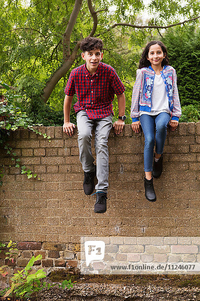 Portrait of brother and sister sitting on wall