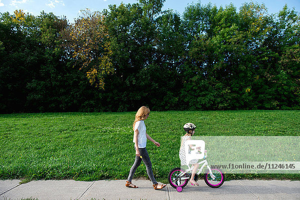 Junges Mädchen fährt Fahrrad  gefolgt von der Mutter