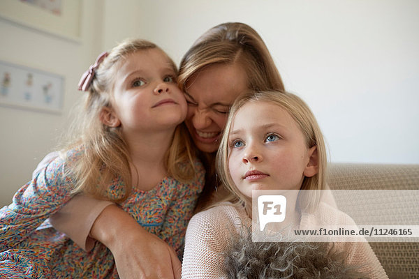Mittlere erwachsene Frau umarmt Töchter im Wohnzimmer