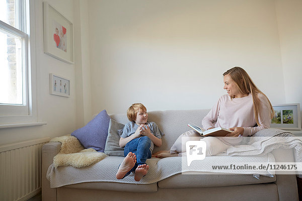 Mittlere erwachsene Frau und Sohn lesen auf dem Sofa ein Märchenbuch