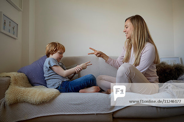 Mittelgroße erwachsene Frau und Sohn spielen Stein-Papier-Schere auf dem Sofa