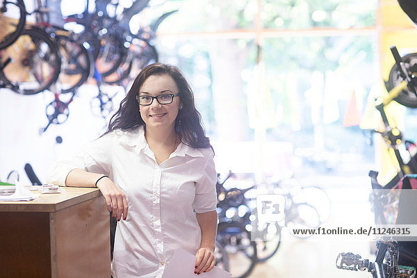 Frau im Fahrradgeschäft lehnt gegen die Ladentheke und schaut lächelnd in die Kamera