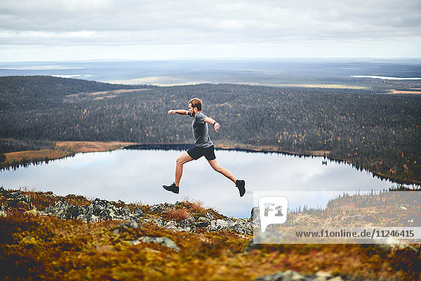 Mann sprintet auf felsigem Klippengipfel  Keimiotunturi  Lappland  Finnland