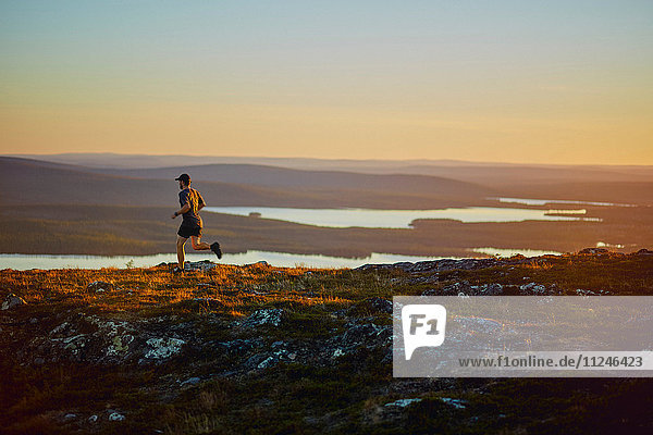 Mann rennt bei Sonnenuntergang auf den Klippen  Keimiotunturi  Lappland  Finnland