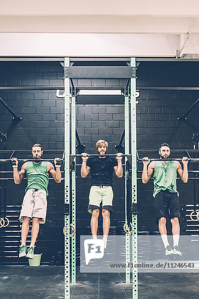 Zwei männliche Crosstrainer machen im Fitnessstudio Kinnübungen an der Übungsstange