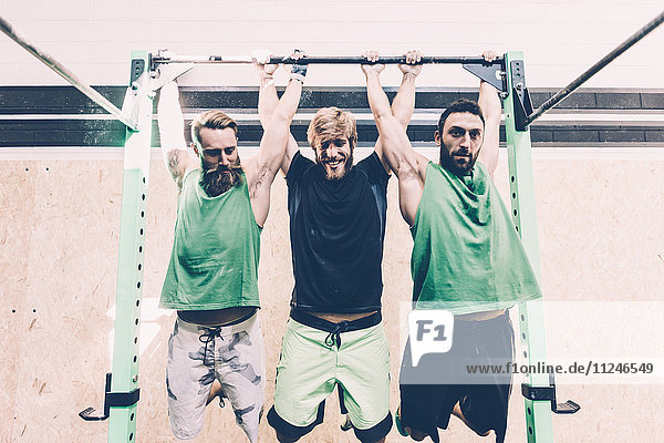 Drei männliche Crosstrainer trainieren im Fitnessstudio an der Stange
