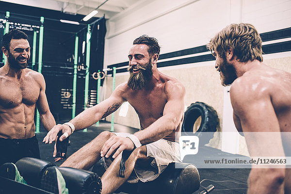 Drei männliche Crosstrainer unterhalten sich im Fitnessstudio