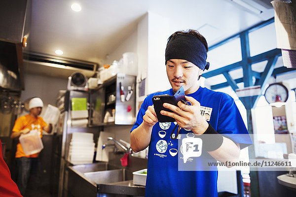 Der Ramen-Nudel-Laden  Personal  das Essen zubereitet. Ein Küchenchef mit einem Smartphone in einer Küche.