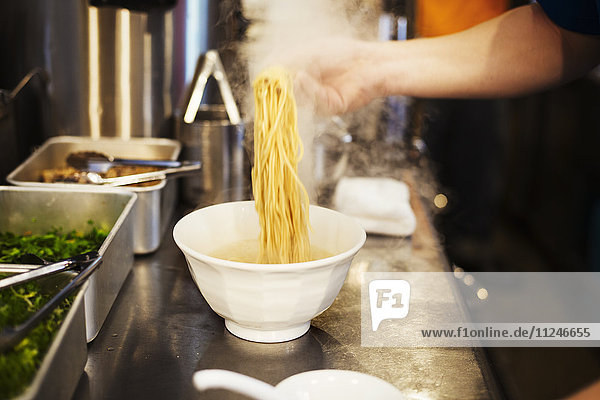 A ramen noodle shop kitchen. A chef preparing bowls of ramen noodles in broth  a speciality and fast food dish.