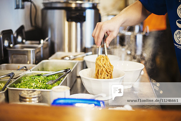A ramen noodle shop kitchen. A chef preparing bowls of ramen noodles in broth  a speciality and fast food dish.