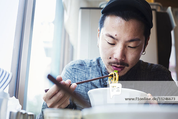 A ramen noodle cafe in a city. A man sitting eating ramen noodle soup dish.