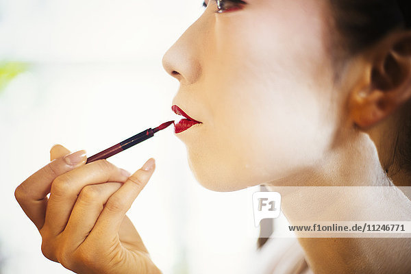 Eine moderne Frau  die mit einem feinen Pinsel auf Lippenstift die traditionellen lebendig roten Lippen der Geishas malt. Weißes Gesichts-Make-up.