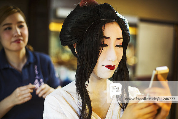 Eine Geisha oder Maiko mit einem Haar- und Make-up-Künstler  der die traditionelle Frisur und das Make-up kreiert.