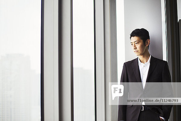 A businessman in the office  by a large window  looking over the city.