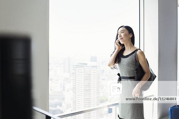 A business woman by a window with a view over the city  using her smart phone.