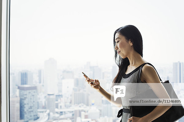 A business woman by a window with a view over the city  using her smart phone.