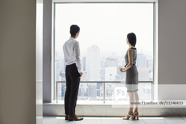 A businessman and businesswoman standing by a large window overlooking a city.