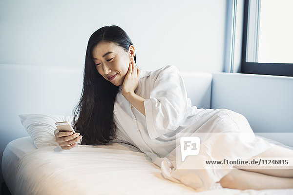 Eine Geschäftsfrau  die sich auf die Arbeit vorbereitet  aufwacht und ihr Smartphone im Bett überprüft.