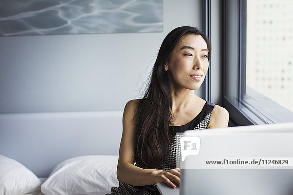 Eine angezogene Geschäftsfrau  die mit einem Laptop auf ihrem Bett sitzt.