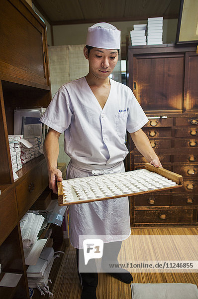 Ein kleiner Kunsthandwerker  der spezielle Leckereien herstellt  Süßigkeiten namens wagashi/ Ein Mann  der ein Tablett mit Süßigkeiten in der Hand hält.