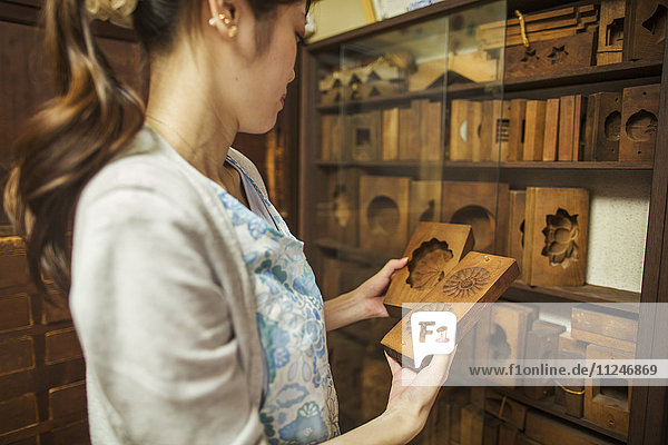 Ein kleiner handwerklicher Hersteller von speziellen Leckereien  Süßigkeiten namens Wagashi. Eine Frau hält geformte Holzformen in der Hand  die bei der Herstellung von Süßigkeiten verwendet werden.