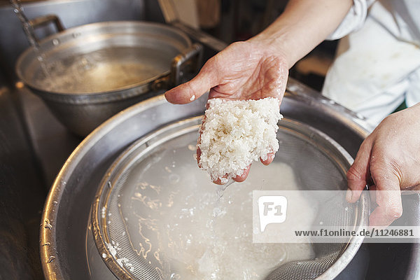 A chef working in a small commercial kitchen  an itamae or master chef making sushi. Preparing rice for the dishes.