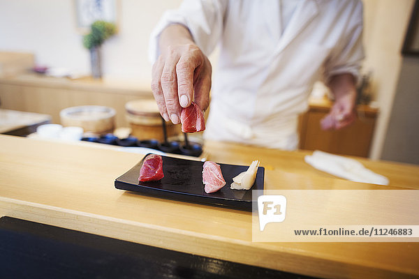 Ein Koch  der in einer kleinen Großküche arbeitet  ein Itamae oder ein Meisterkoch  der einen frischen Sushi-Teller präsentiert.