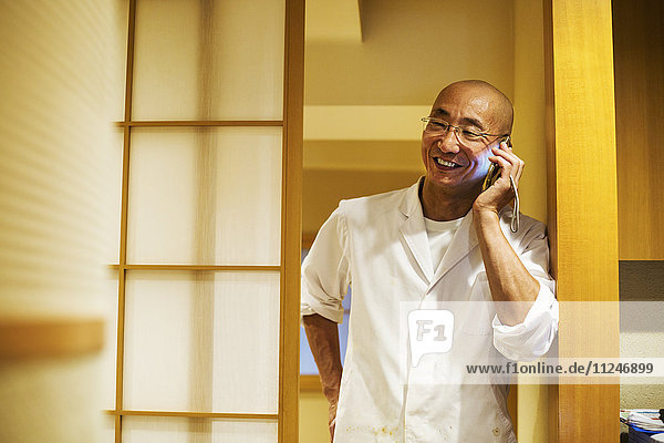 Ein Koch in einer kleinen Großküche  ein Itamae oder ein Meisterkoch auf seinem Smartphone.